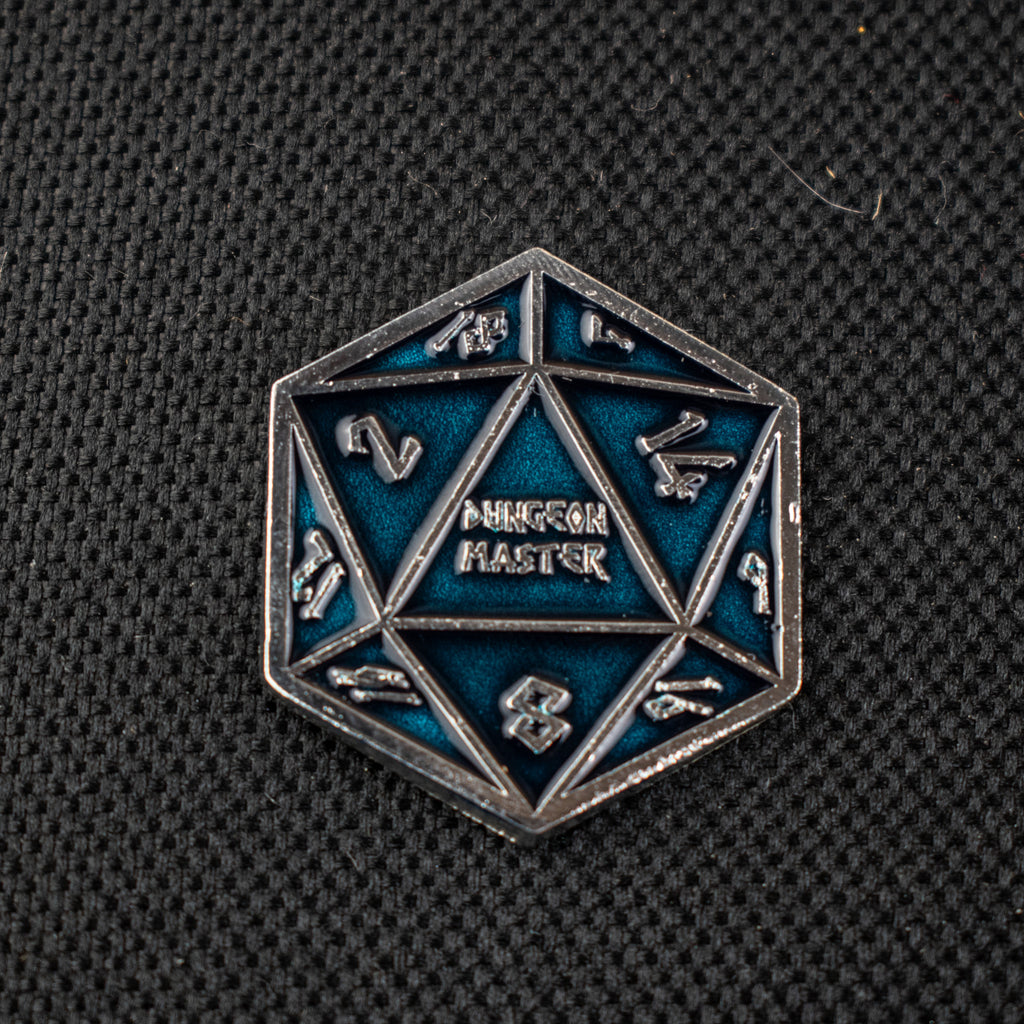 An aqua D20 pin with silver numbers in a Nordic font and "Dungeon Master" in the middle