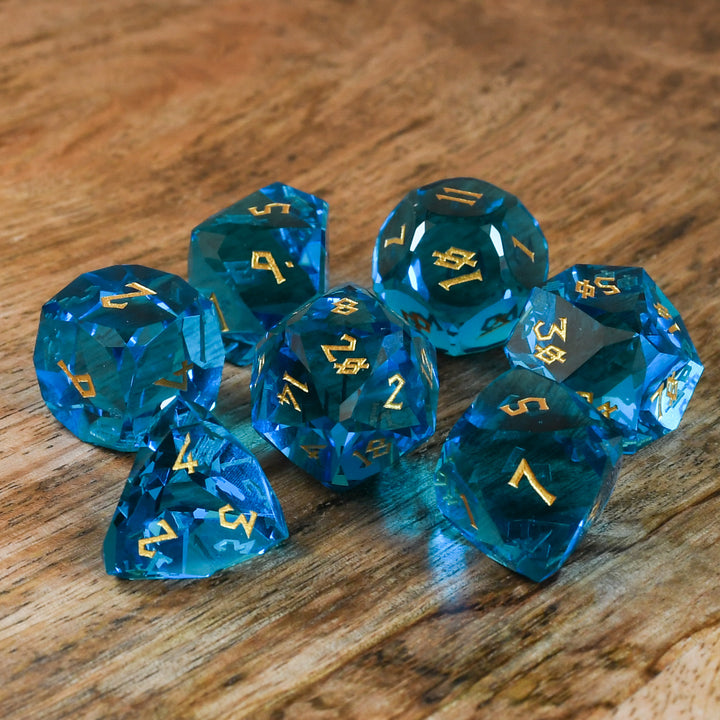 A set of multifaceted blue glass dice with engraved numbers, displayed on a wooden surface.
