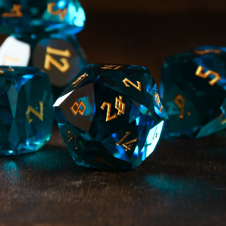 A set of multifaceted blue glass dice with engraved numbers, displayed on a wooden surface.