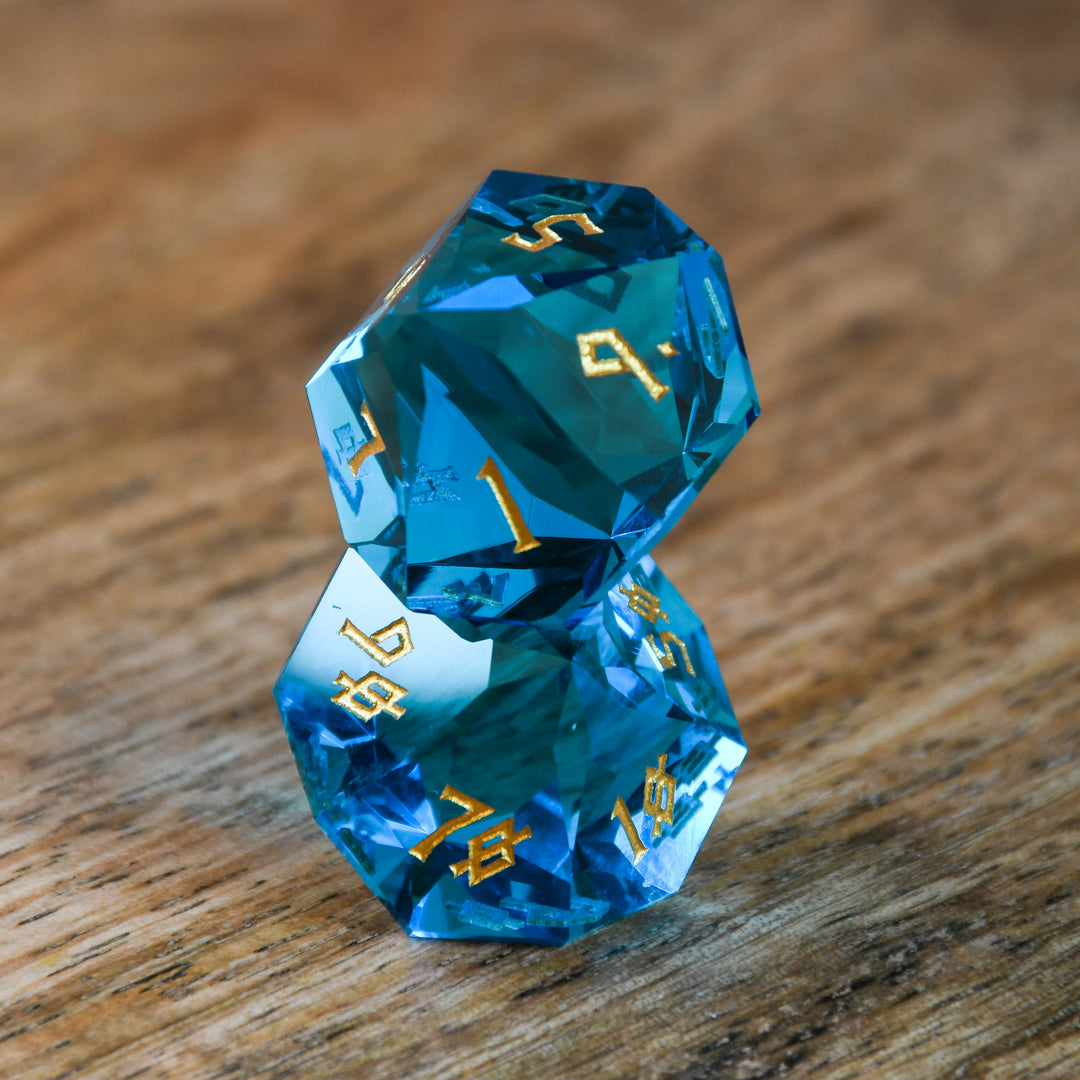 A set of multifaceted blue glass dice with engraved numbers, displayed on a wooden surface.