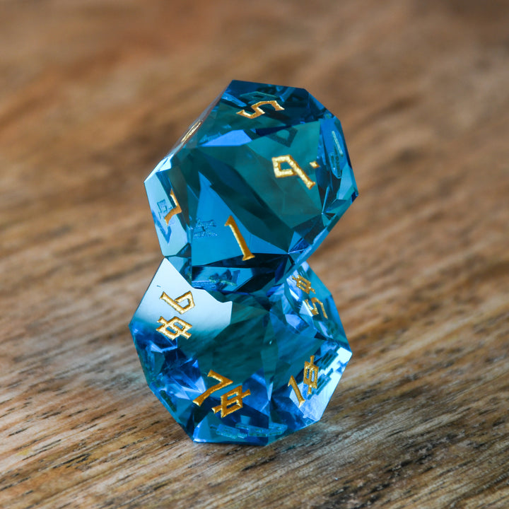 A set of multifaceted blue glass dice with engraved numbers, displayed on a wooden surface.