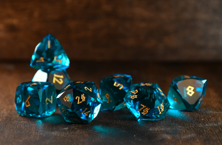 A set of multifaceted blue glass dice with engraved numbers, displayed on a wooden surface.