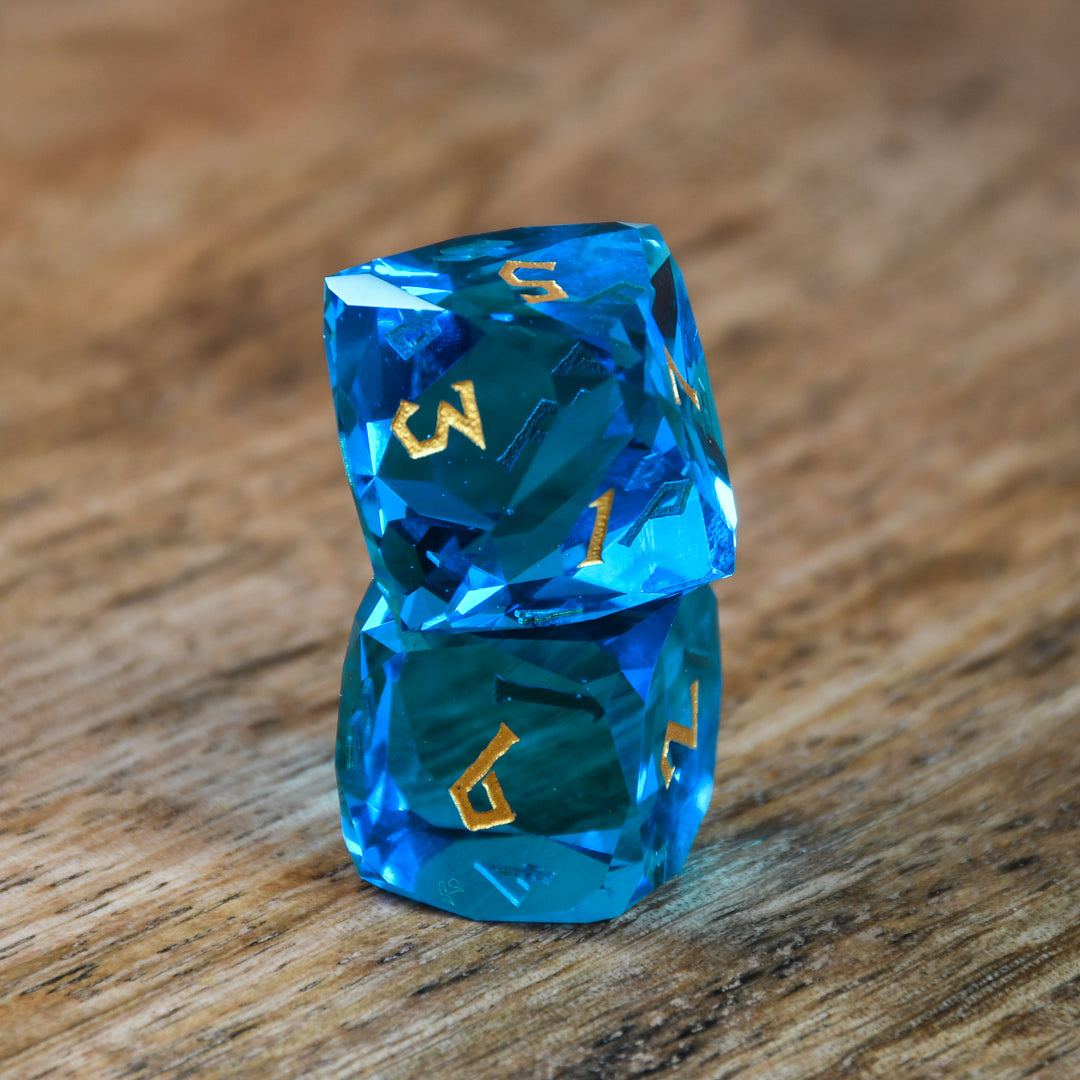 A set of multifaceted blue glass dice with engraved numbers, displayed on a wooden surface.