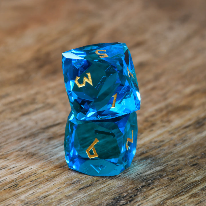 A set of multifaceted blue glass dice with engraved numbers, displayed on a wooden surface.
