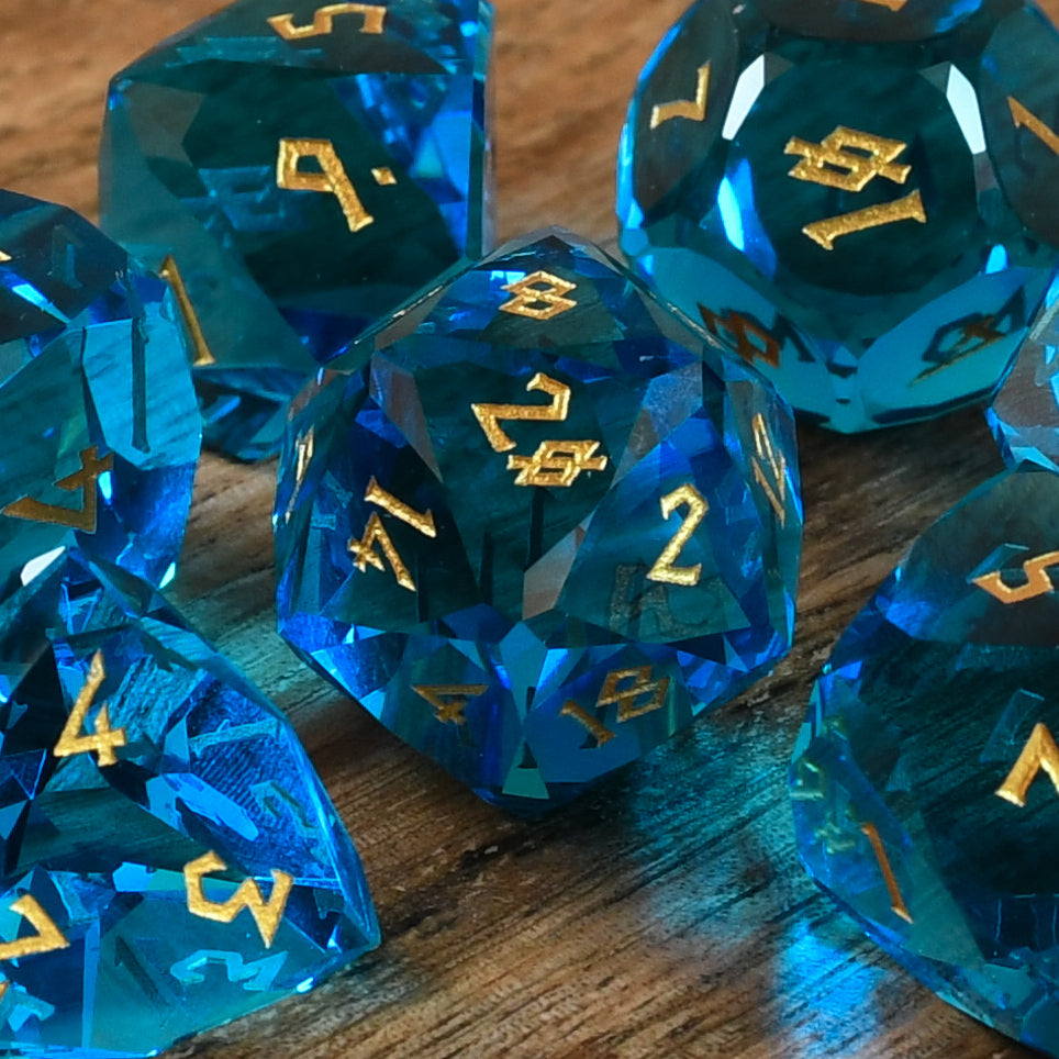 A set of multifaceted blue glass dice with engraved numbers, displayed on a wooden surface.