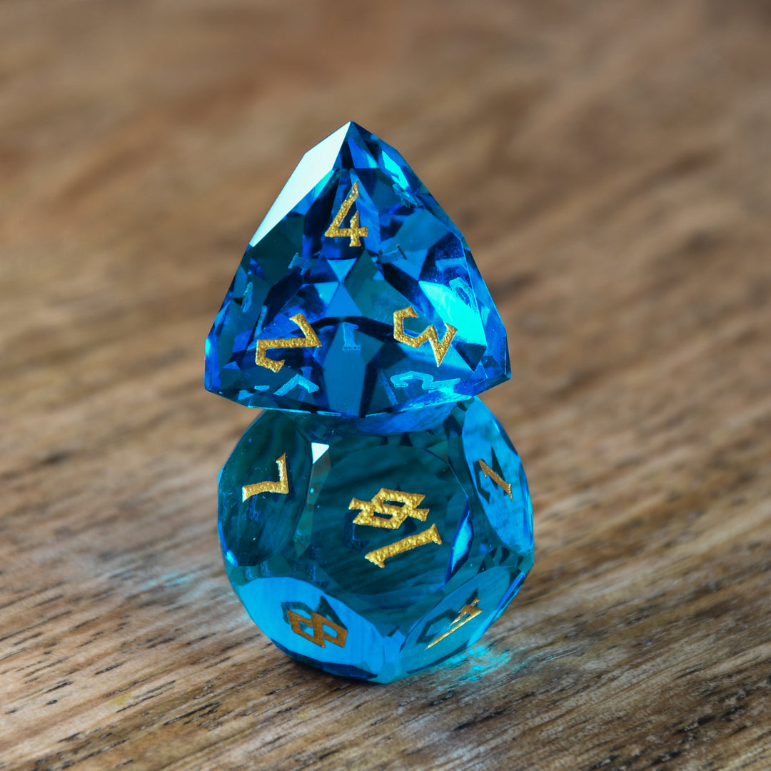 A set of multifaceted blue glass dice with engraved numbers, displayed on a wooden surface.