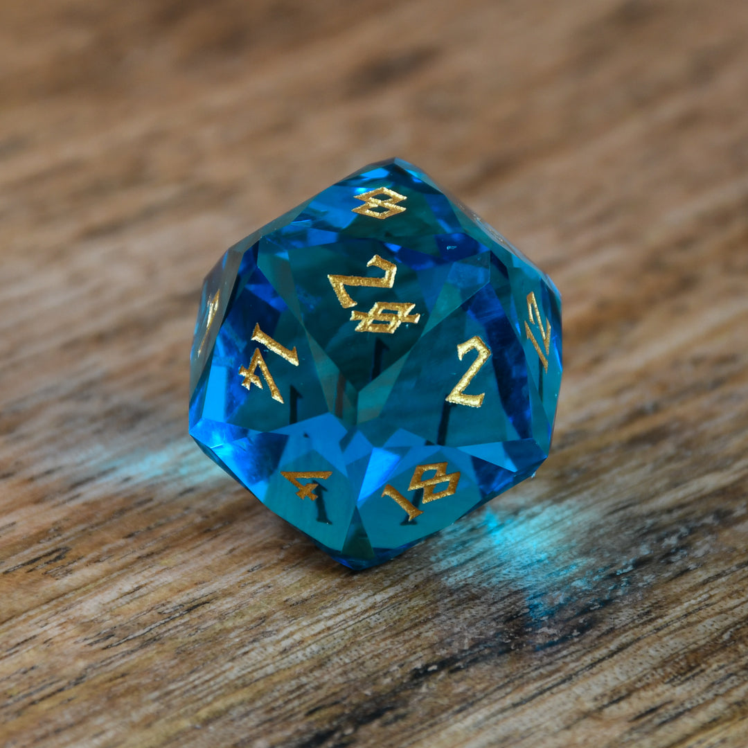A set of multifaceted blue glass dice with engraved numbers, displayed on a wooden surface.