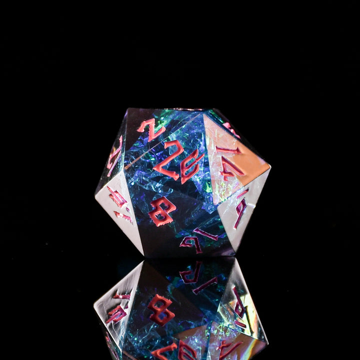 A set of sharp-edged, multicolored resin polyhedral dice with hand-painted pink numbers, with iridescent foil inside reflecting in a mirrored surface.