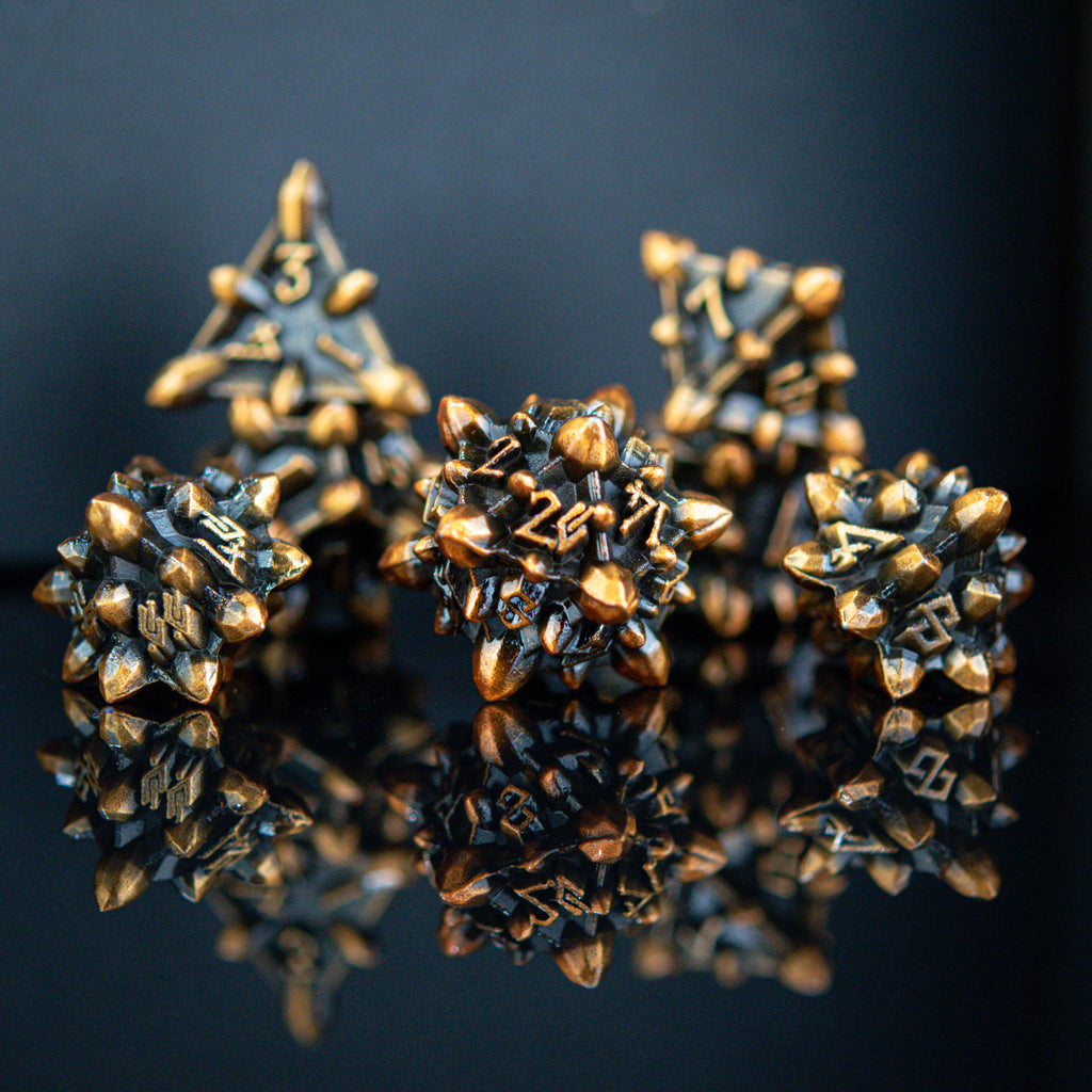A set of metal dice with an asteroid-like texture, featuring weathered bronze and gold colors, displayed on a reflective surface.