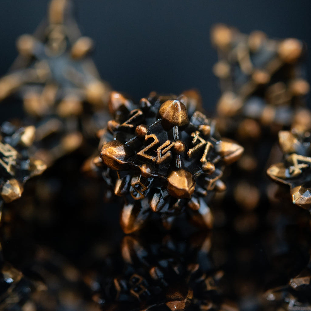A set of metal dice with an asteroid-like texture, featuring weathered bronze and gold colors, displayed on a reflective surface.