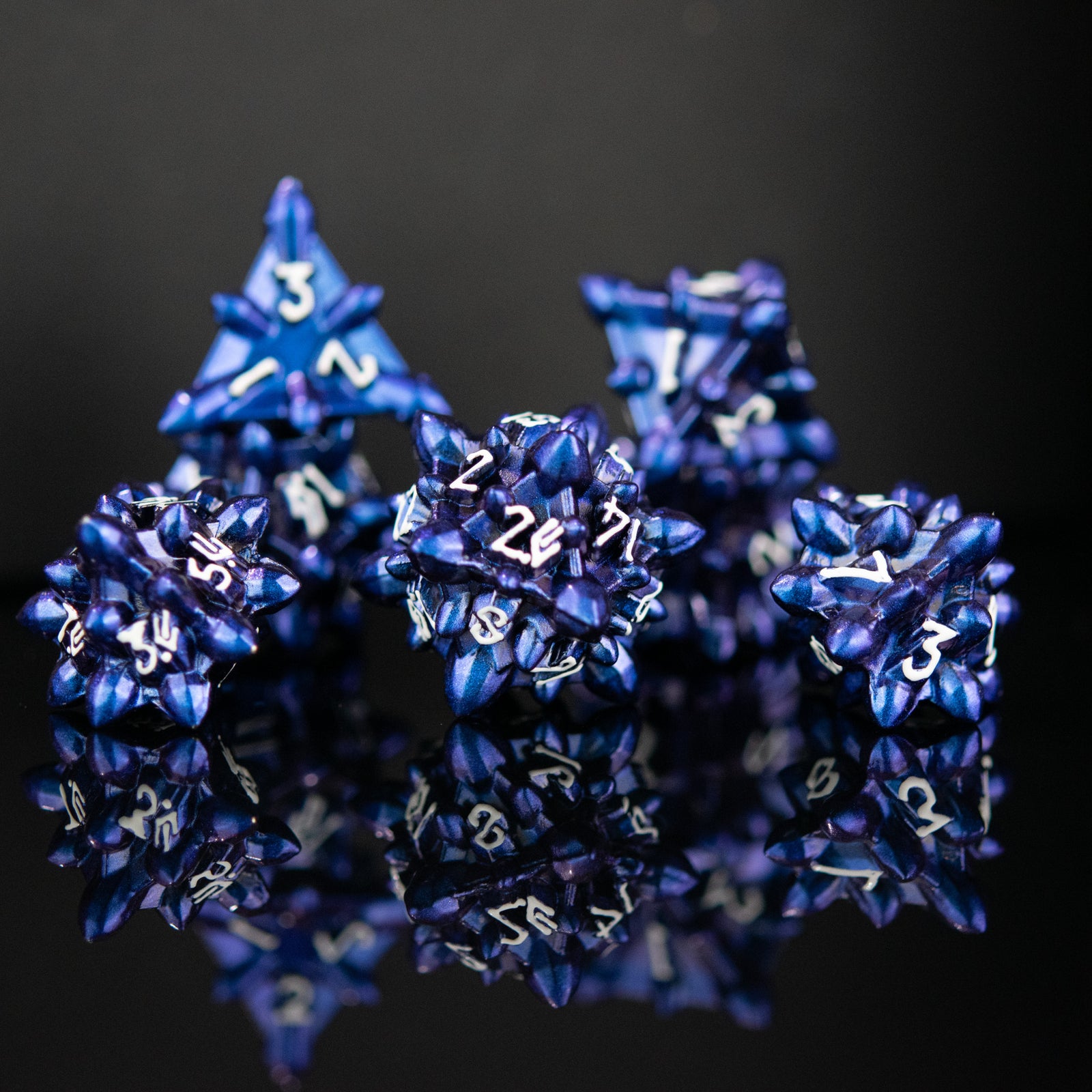A set of blue metal dice with embossed white numbers, designed to resemble asteroid shapes, displayed on a reflective surface.