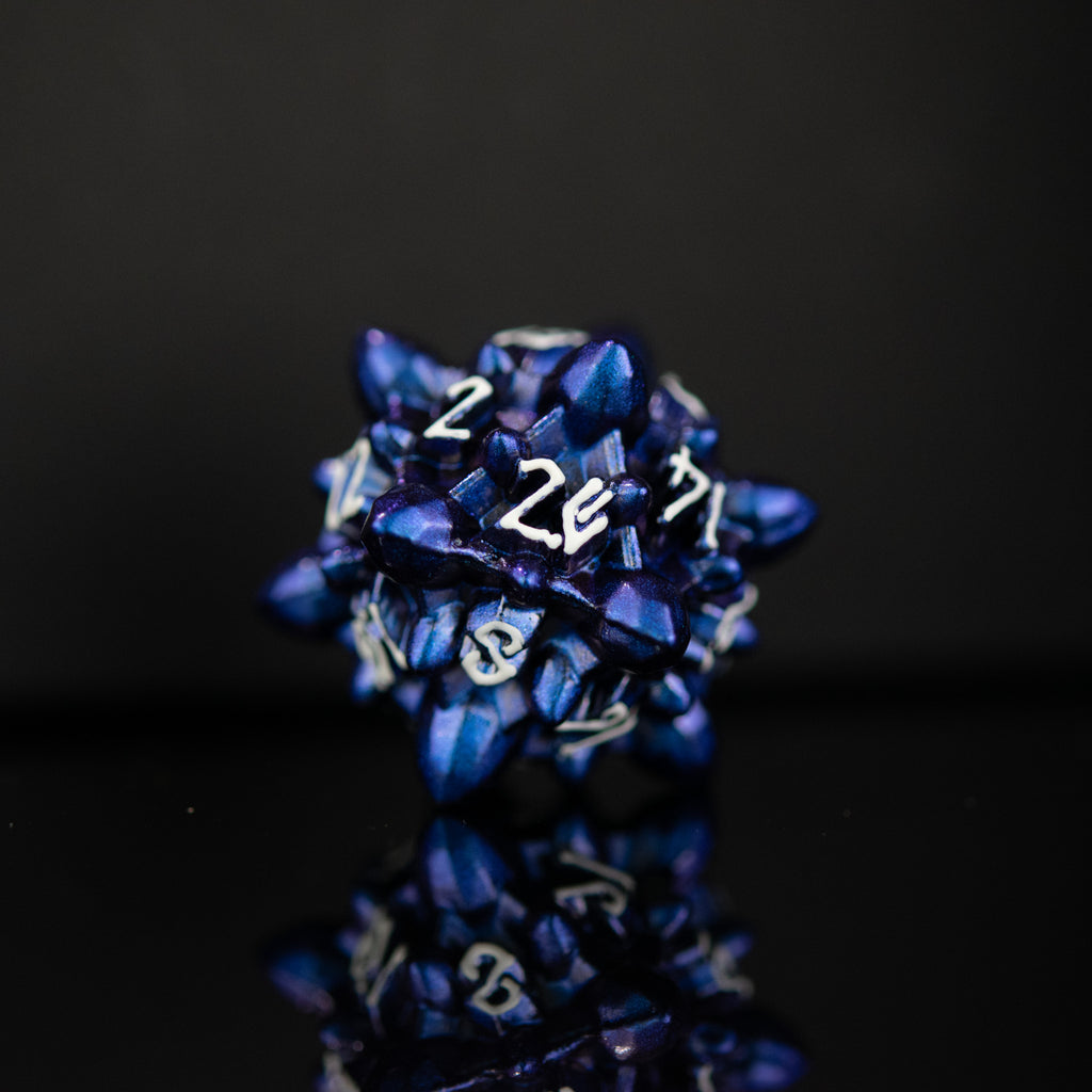blue metal d20 dice with embossed white numbers, designed to resemble asteroid shapes, displayed on a reflective surface.