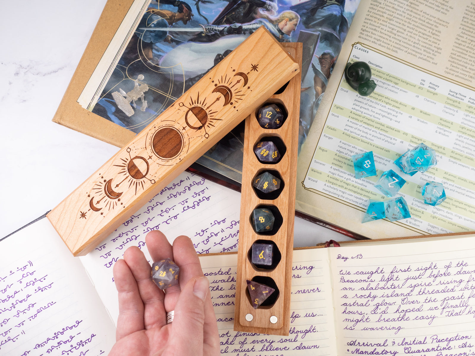 Wooden dice holder with engraved celestial designs on a surface with books and papers.