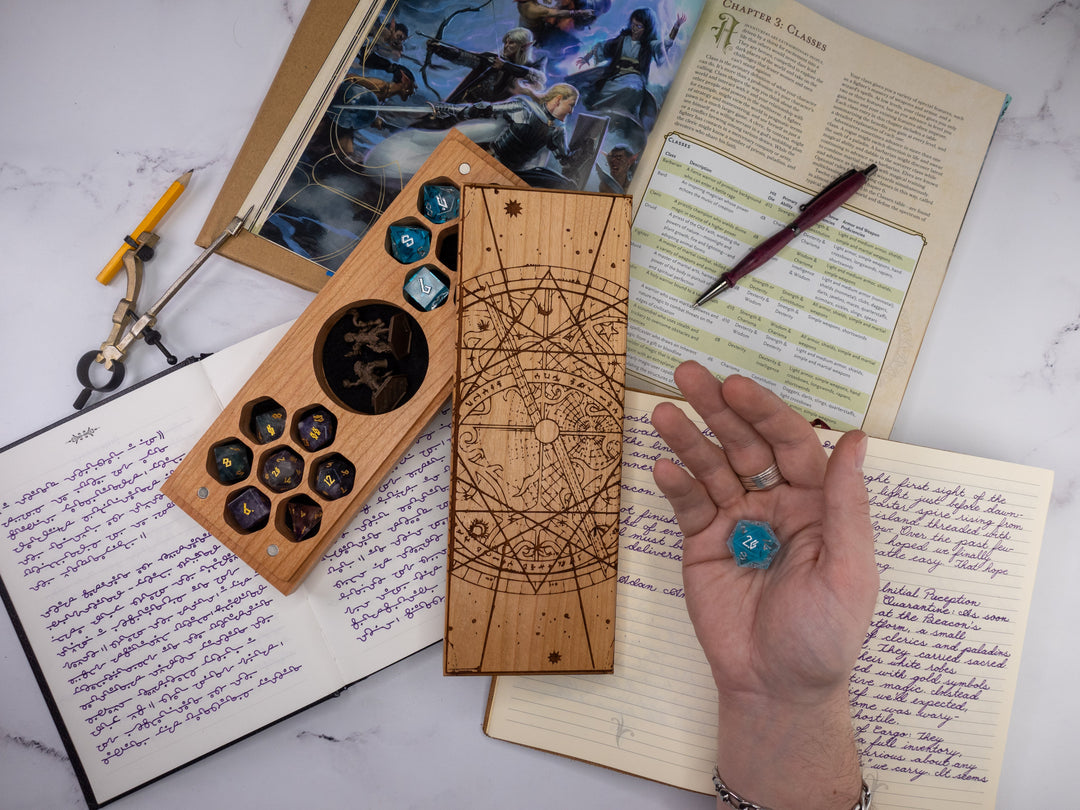 Wooden dice tray with engraved designs on top of a notebook with writing and a pen.