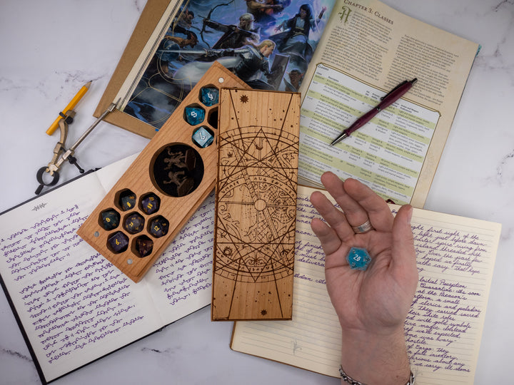 Wooden dice tray with engraved designs on top of a notebook with writing and a pen.