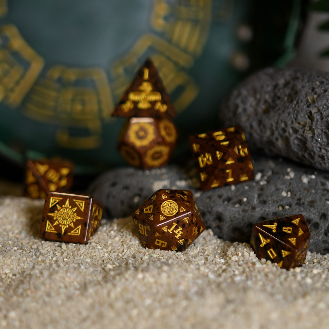 A set of hand-carved, Aztec Mahogany Obsidian Stone Dice with intricate Aztec designs, displayed on a bed of sand.