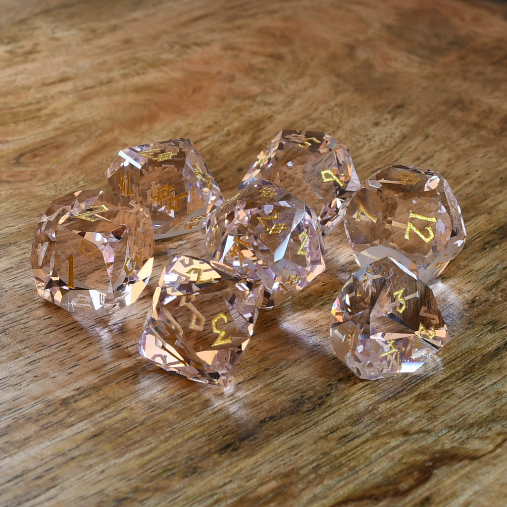 Baby Pink Topaz Multifaceted Glass Dice with gold numbering on wooden surface. 