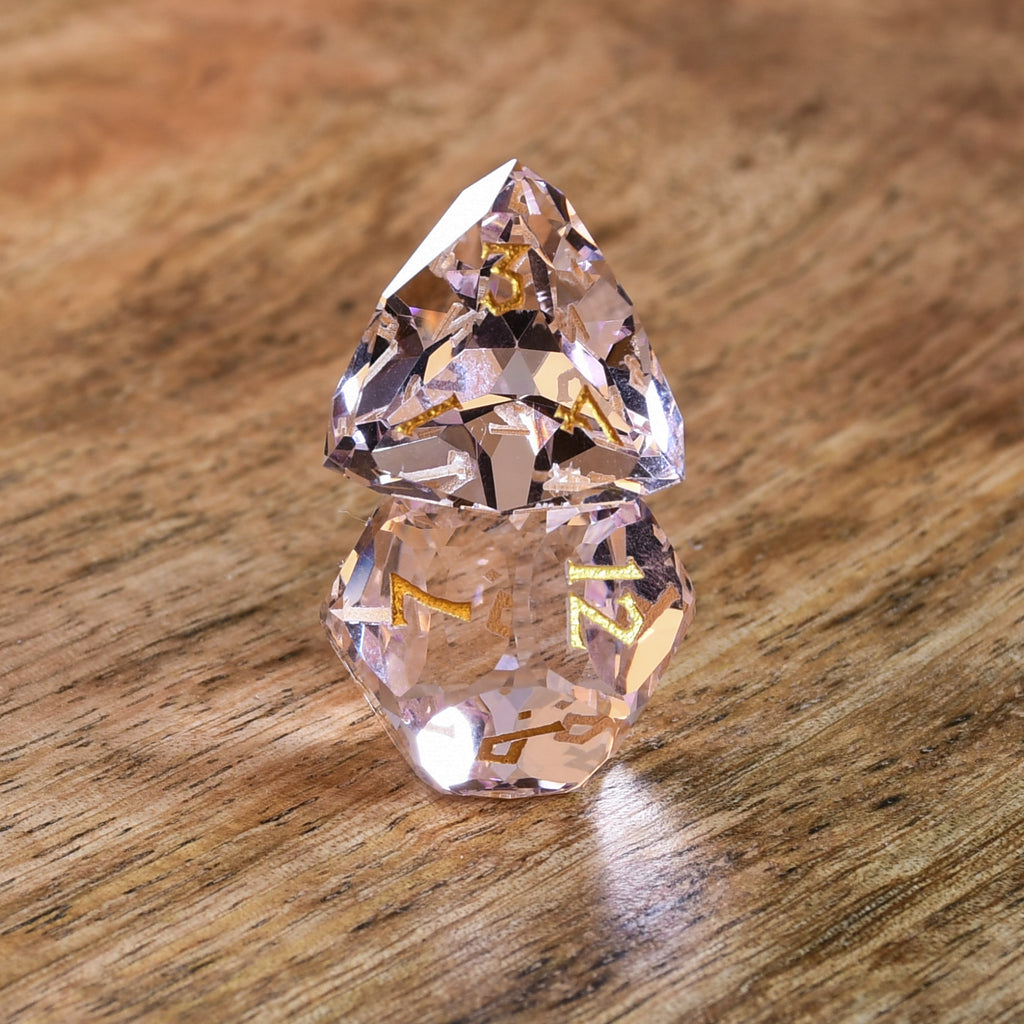 Baby Pink Topaz Multifaceted Glass Dice with gold numbering on wooden surface. 