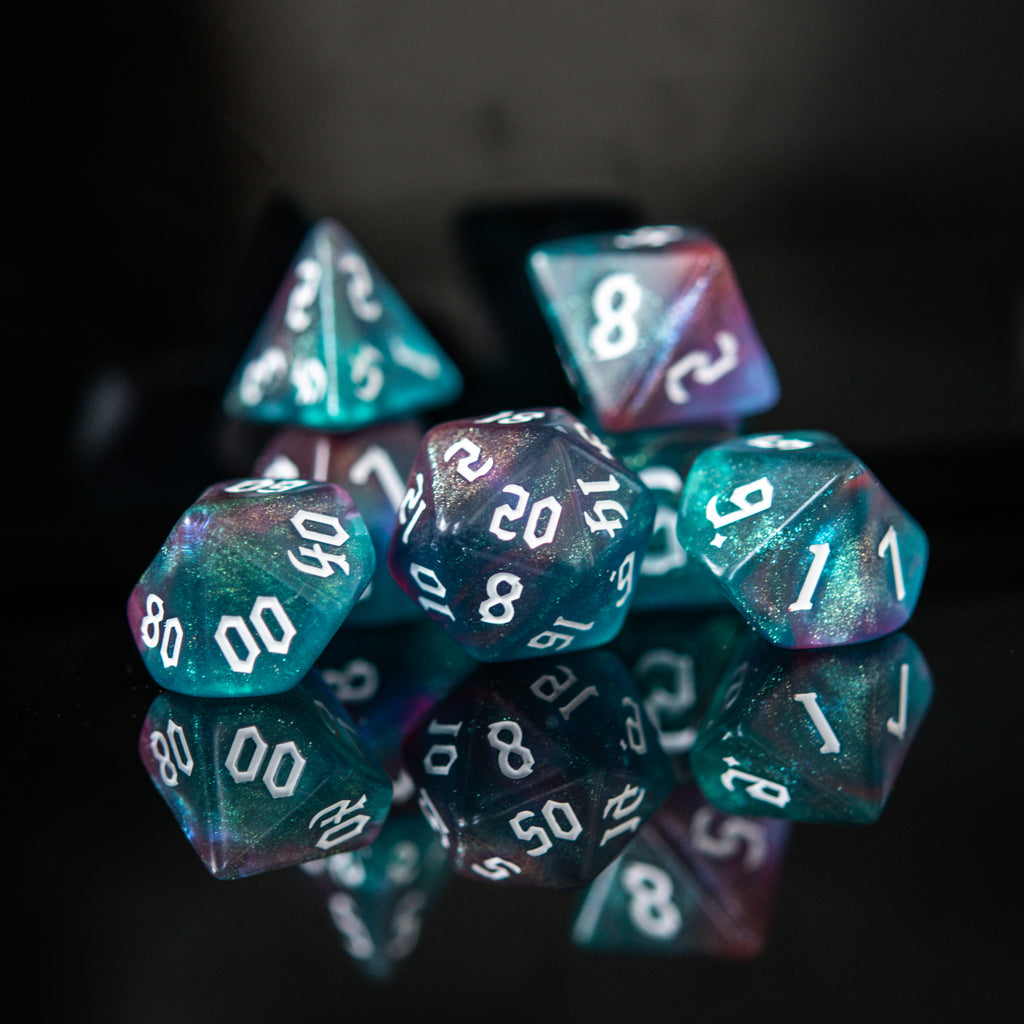 A set of multicolored acrylic dice with engraved numbers, displayed on a reflective surface.