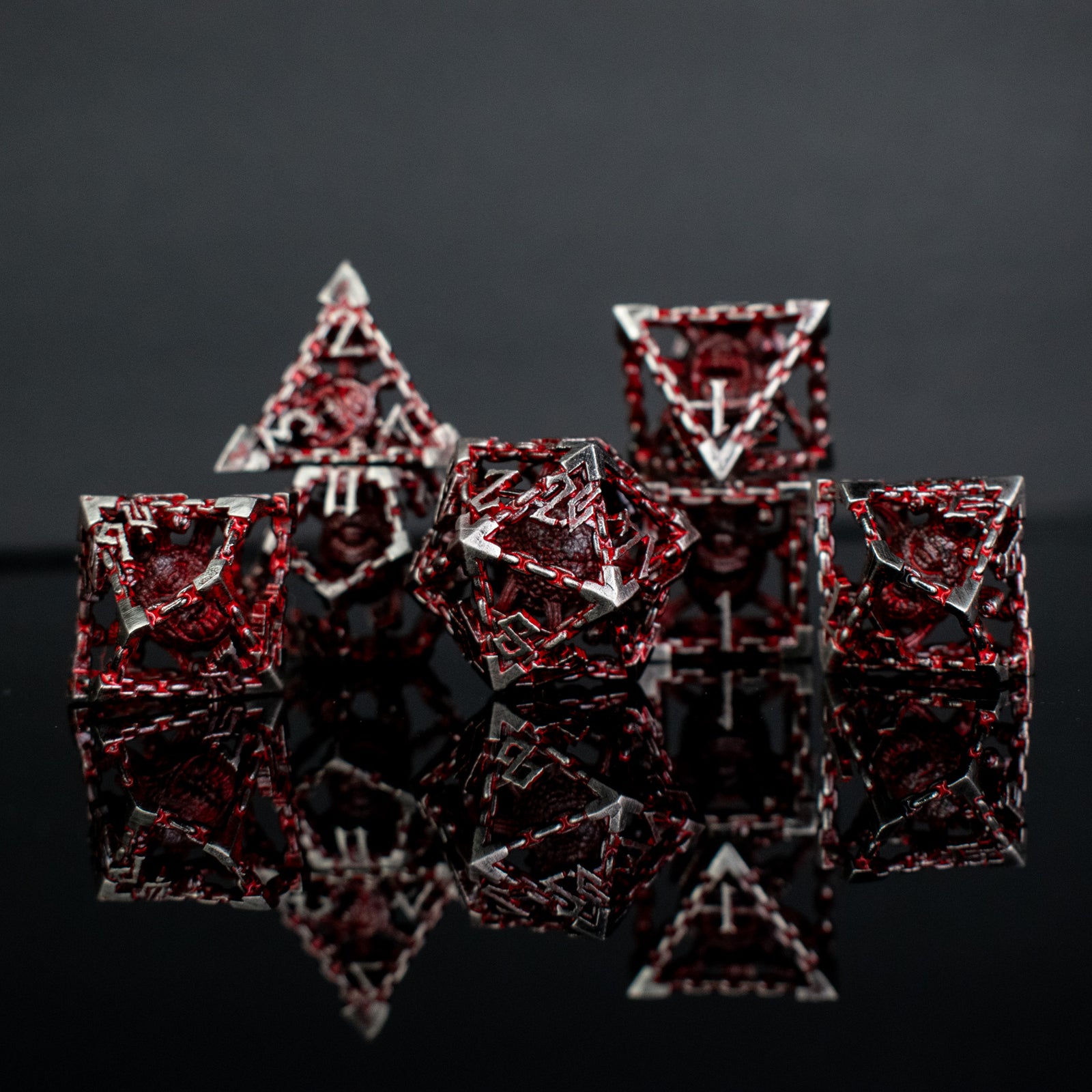 A set of embossed metal dice in silver color with red accents, displayed on a reflective surface.