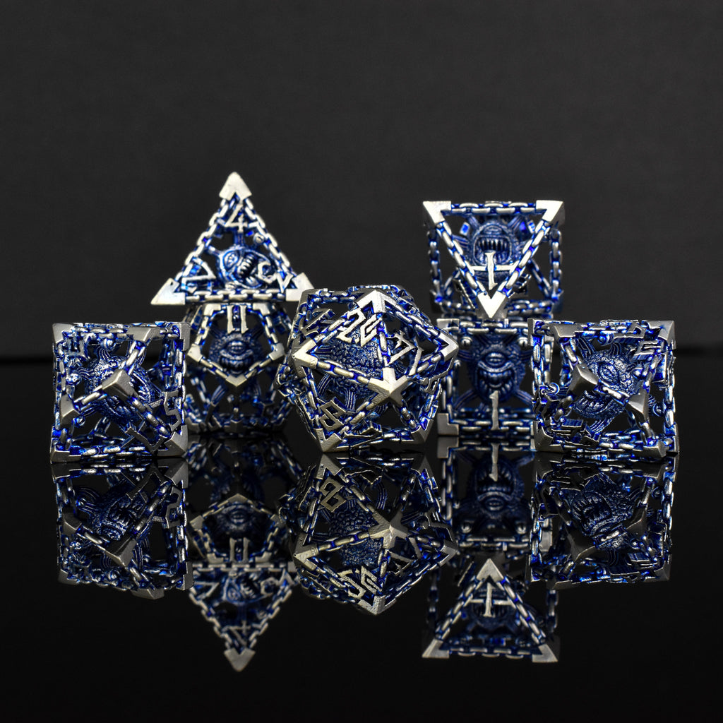 A set of hollow metal dice in blue and silver colors with embossed numbers, reflecting on a dark surface.
