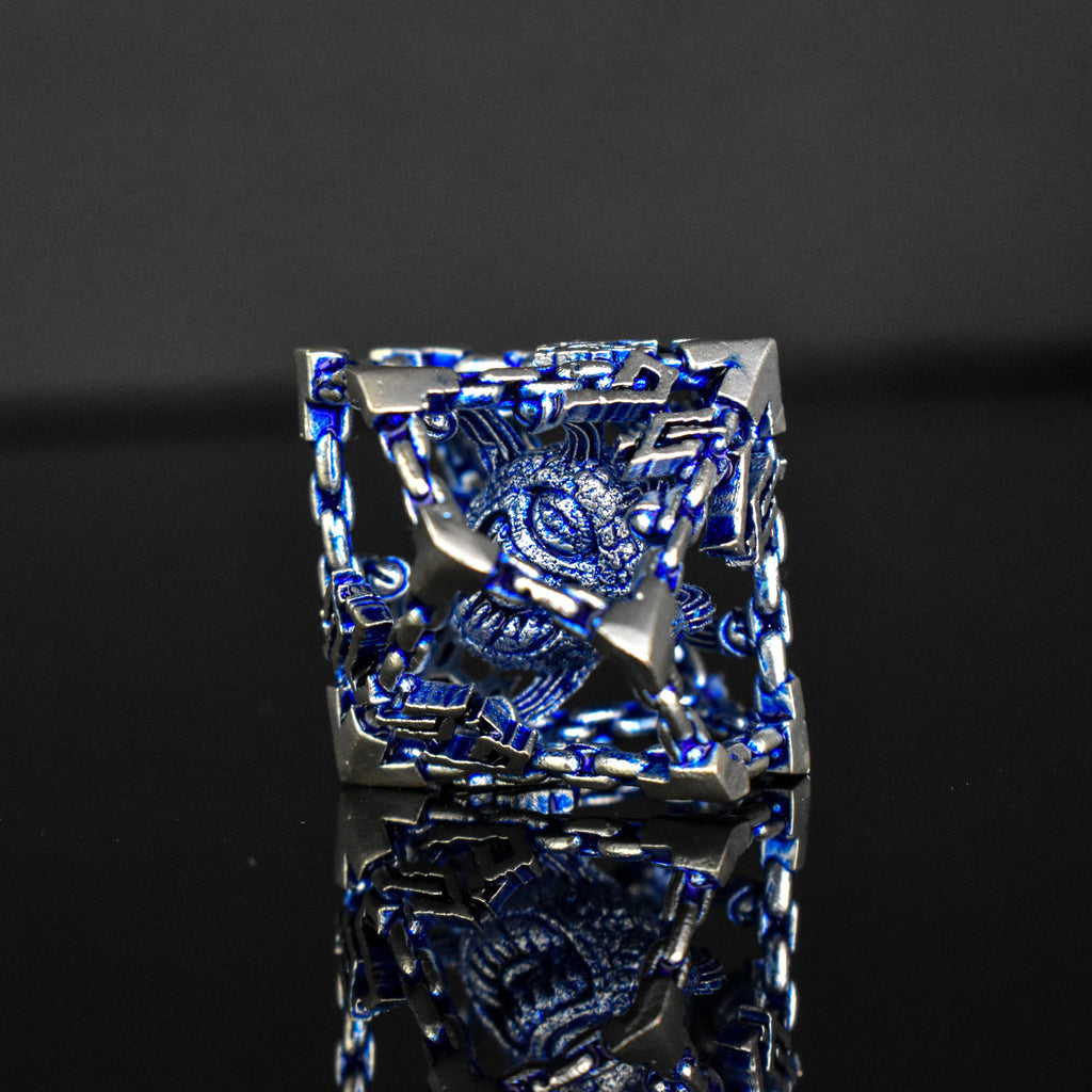 A set of hollow metal dice in blue and silver colors with embossed numbers, reflecting on a dark surface.