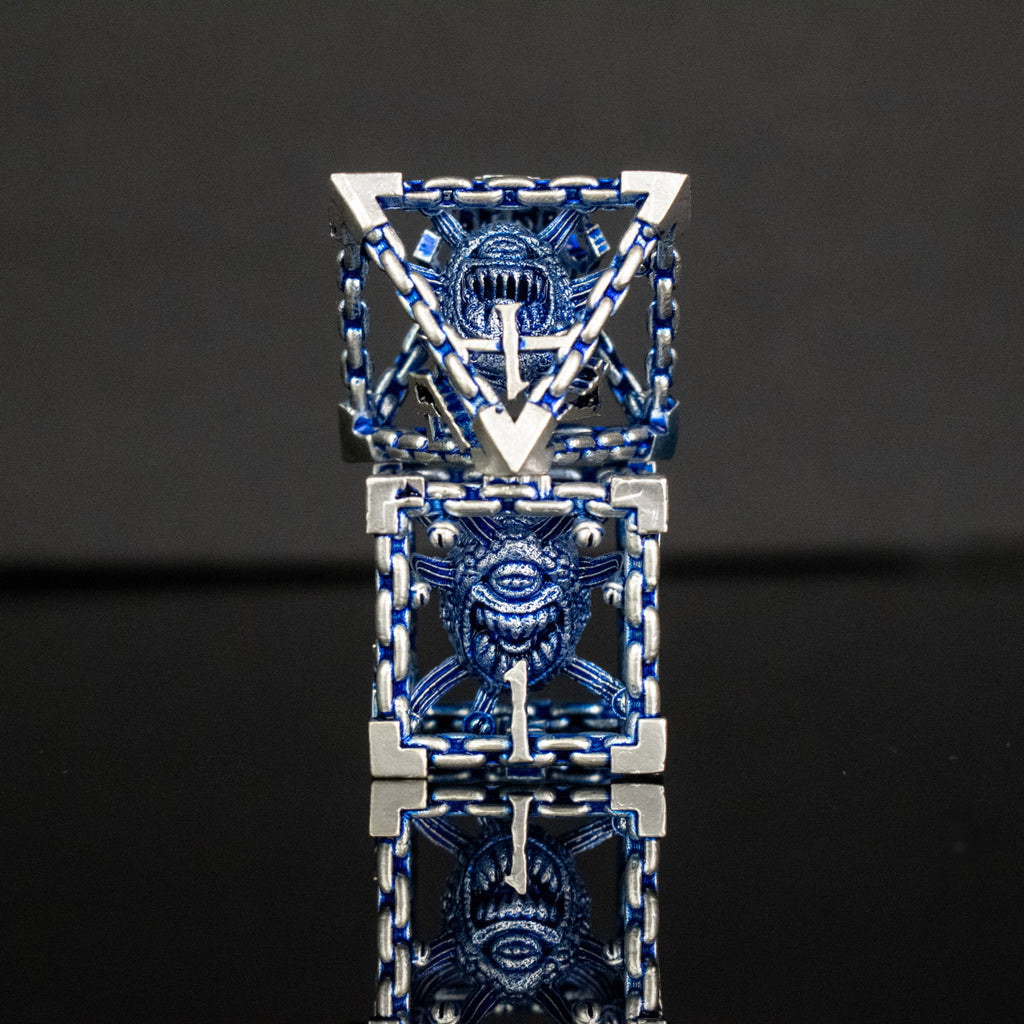 A set of hollow metal dice in blue and silver colors with embossed numbers, reflecting on a dark surface.