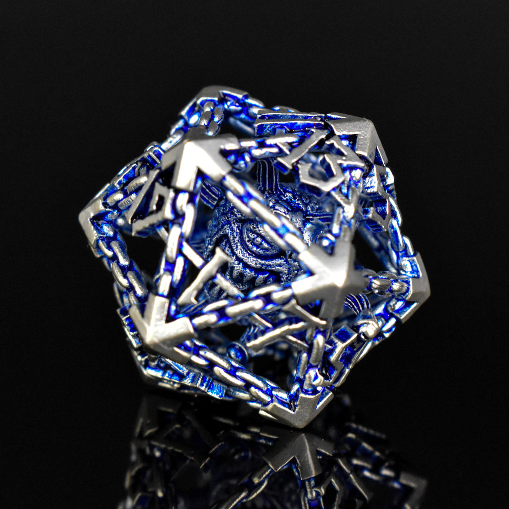 A set of hollow metal dice in blue and silver colors with embossed numbers, reflecting on a dark surface.