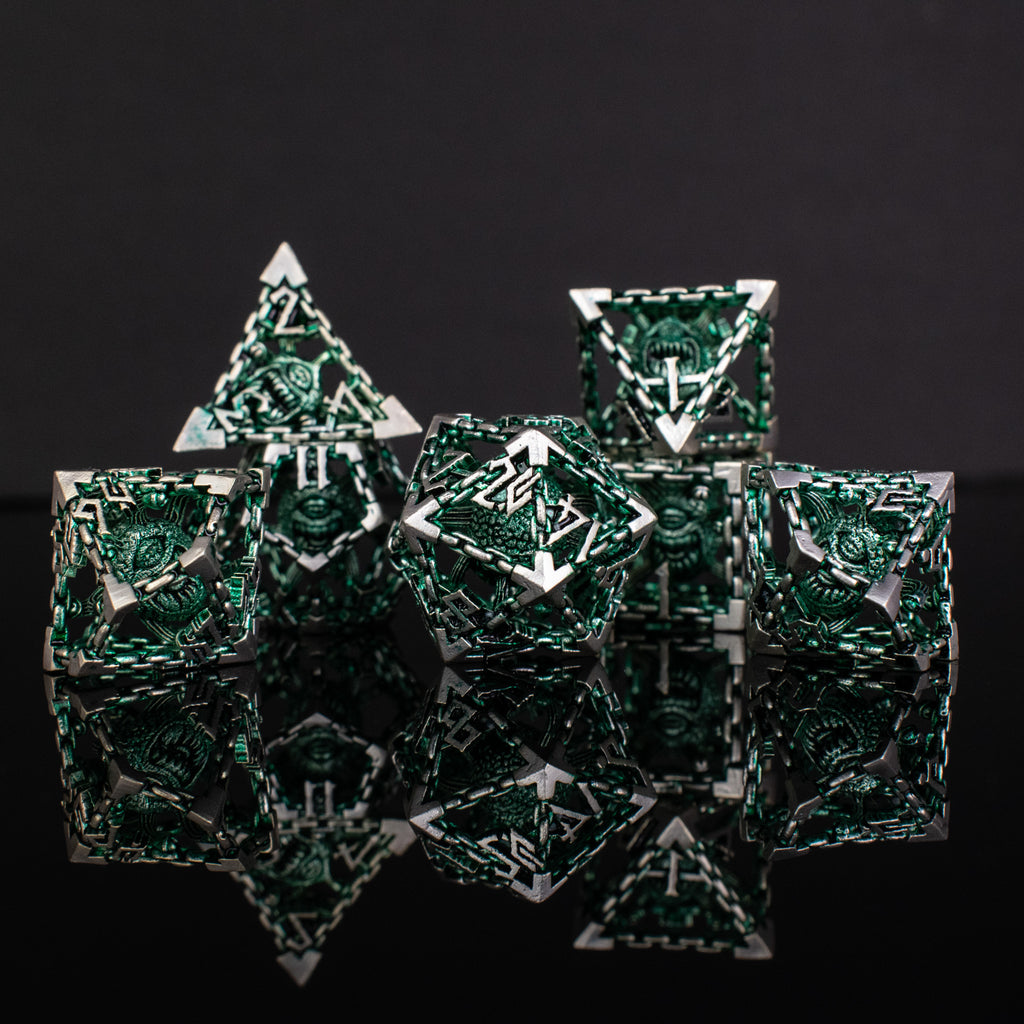A set of hollow metal dice in green and silver colors with embossed numbers, reflecting on a black surface.