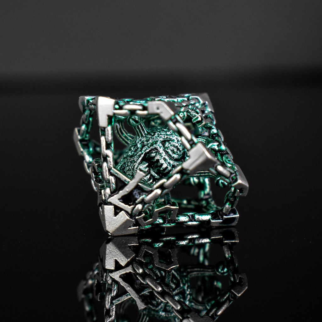 A set of hollow metal dice in green and silver colors with embossed numbers, reflecting on a black surface.
