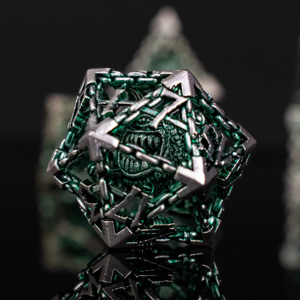 A set of hollow metal dice in green and silver colors with embossed numbers, reflecting on a black surface.