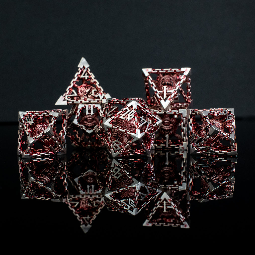 A set of hollow metal dice in red and silver, including various shapes such as a d4, d6, d8, d10, d12, and d20, displayed on a reflective surface.