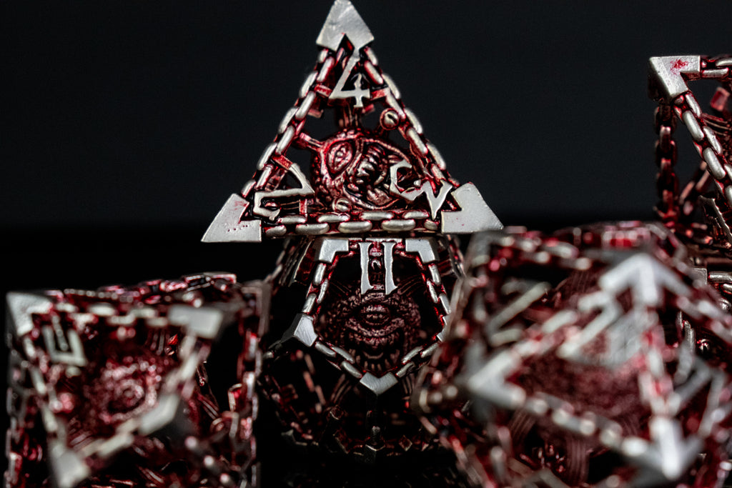 A set of hollow metal dice in red and silver, including various shapes such as a d4, d6, d8, d10, d12, and d20, displayed on a reflective surface.