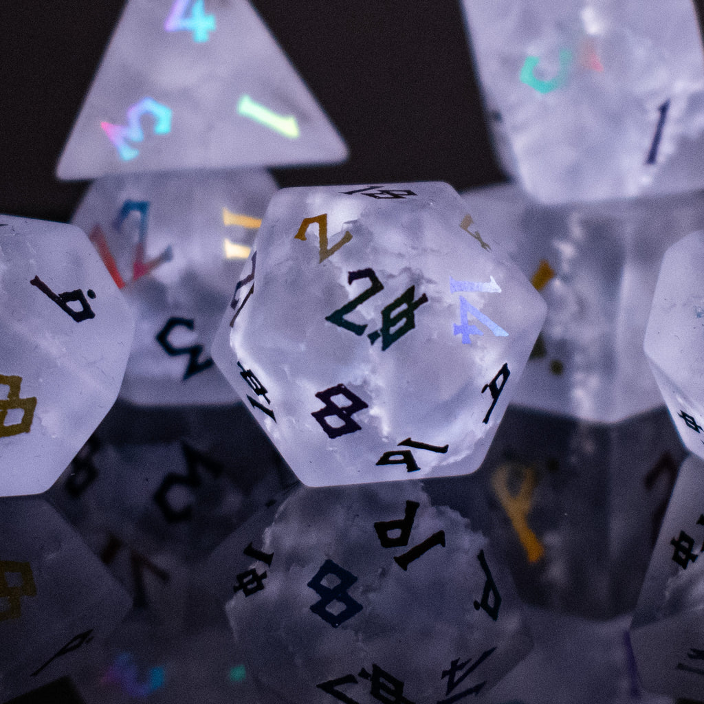 A collection of hand-carved, clear lavender glass dice with engraved numbers, illuminated by a light, displaying a Shattered Glass effect.