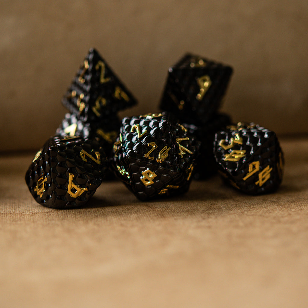 A set of black metal dice with embossed numbers, including various shapes such as a d4, d6, d8, d10, d12, and d20, displayed on a textured surface.