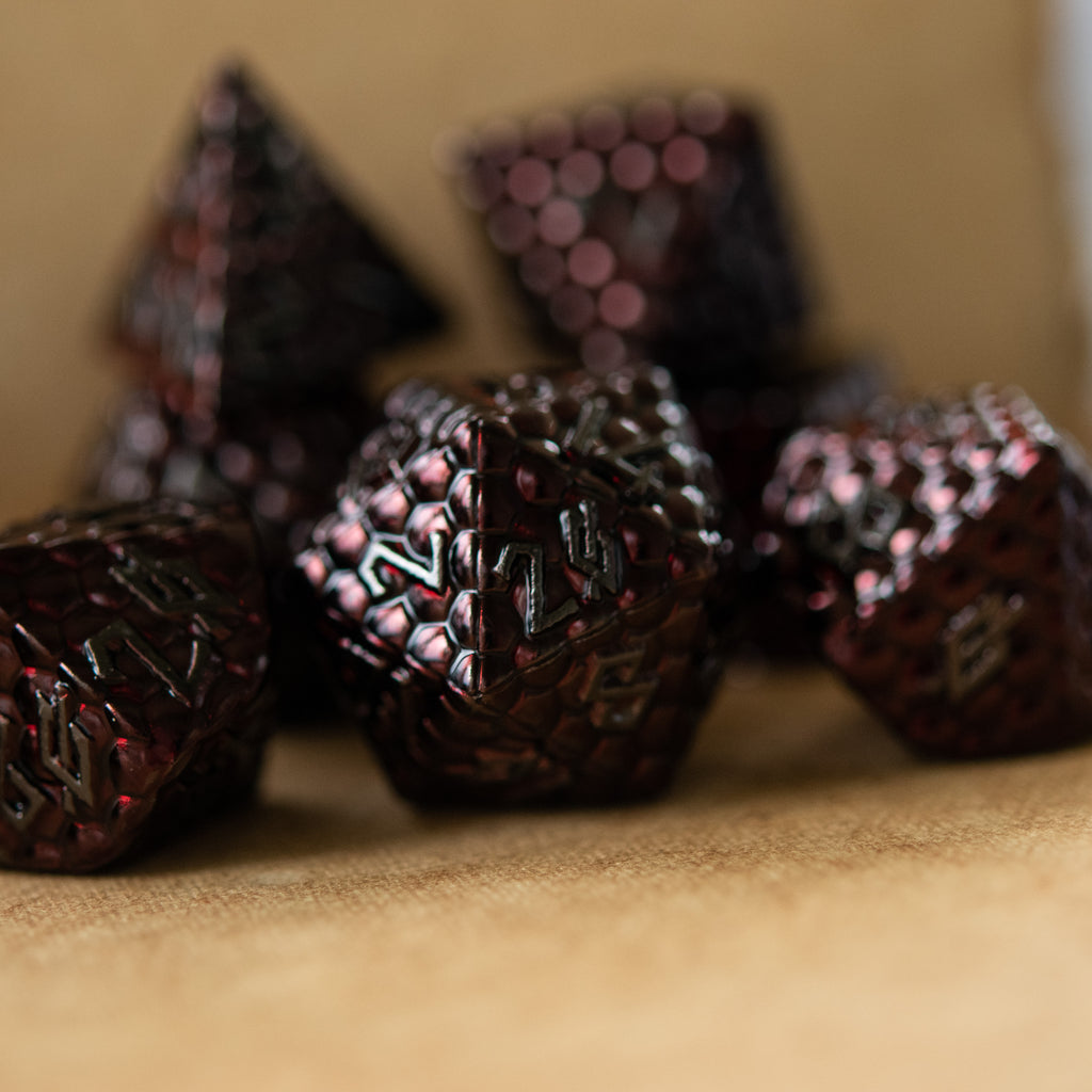 A set of metal dragons egg texture dice in dark red colors with embossed numbers, including various shapes such as a d4, d6, d8, d10, d12, and d20.