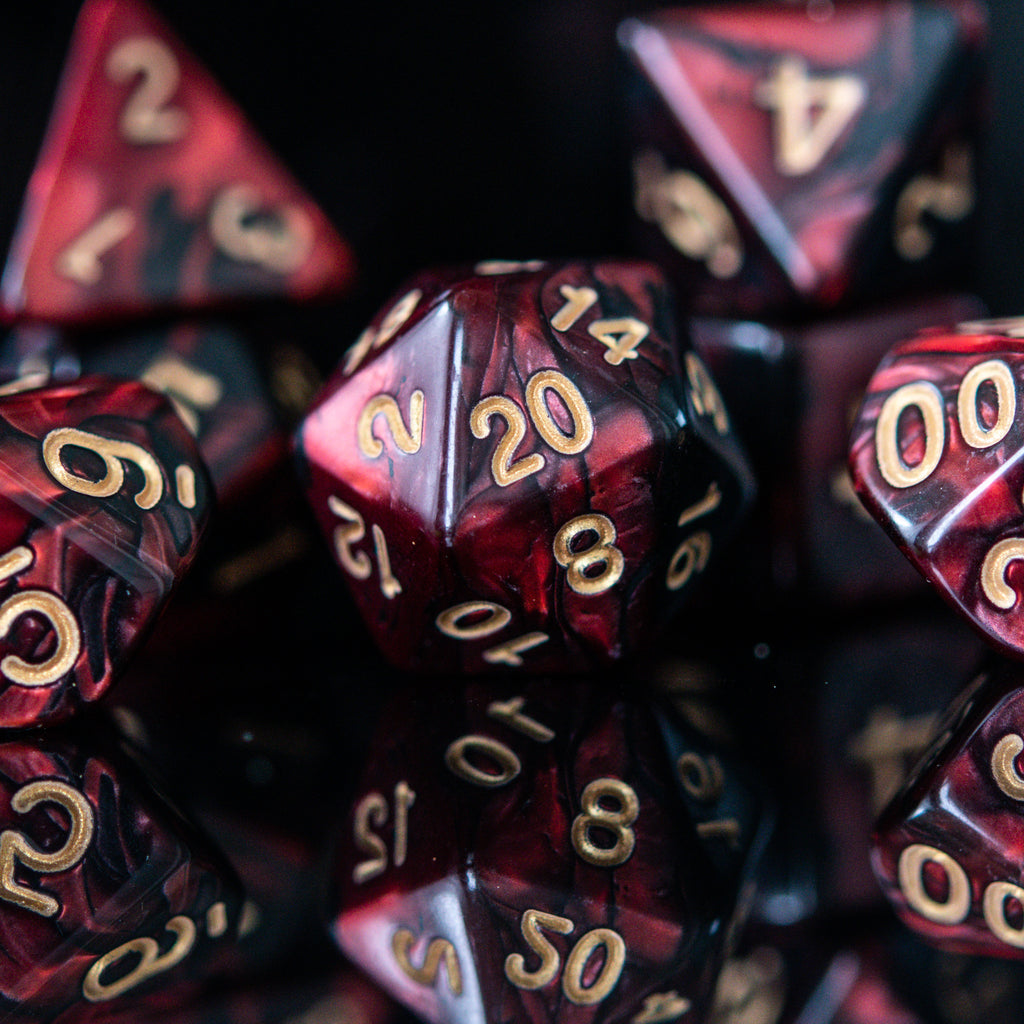 A set of acrylic dice in red and black colors with engraved numbers, including various shapes such as a d4, d6, d8, d10, d12, and d20, commonly used for role-playing games.