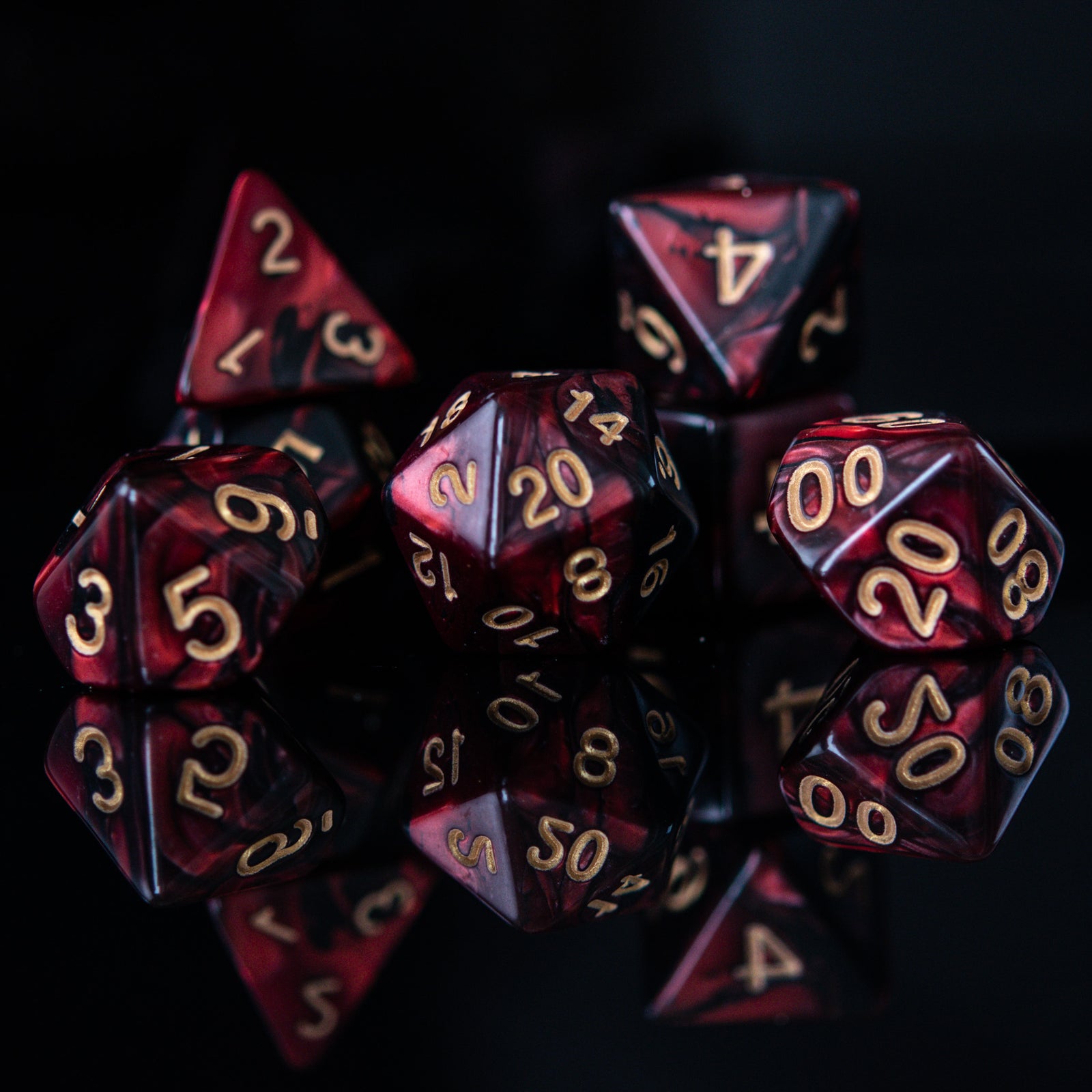 A set of acrylic dice in red and black colors with engraved numbers, including various shapes such as a d4, d6, d8, d10, d12, and d20, commonly used for role-playing games.