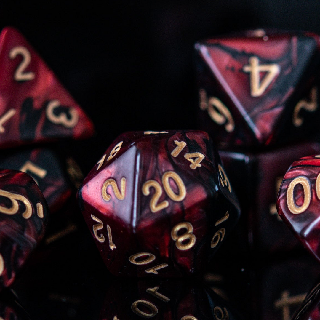 A set of acrylic dice in red and black colors with engraved numbers, including various shapes such as a d4, d6, d8, d10, d12, and d20, commonly used for role-playing games. 