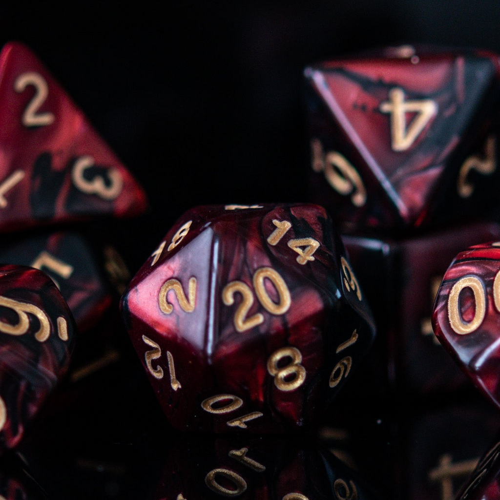 A set of acrylic dice in red and black colors with engraved numbers, including various shapes such as a d4, d6, d8, d10, d12, and d20, commonly used for role-playing games. 