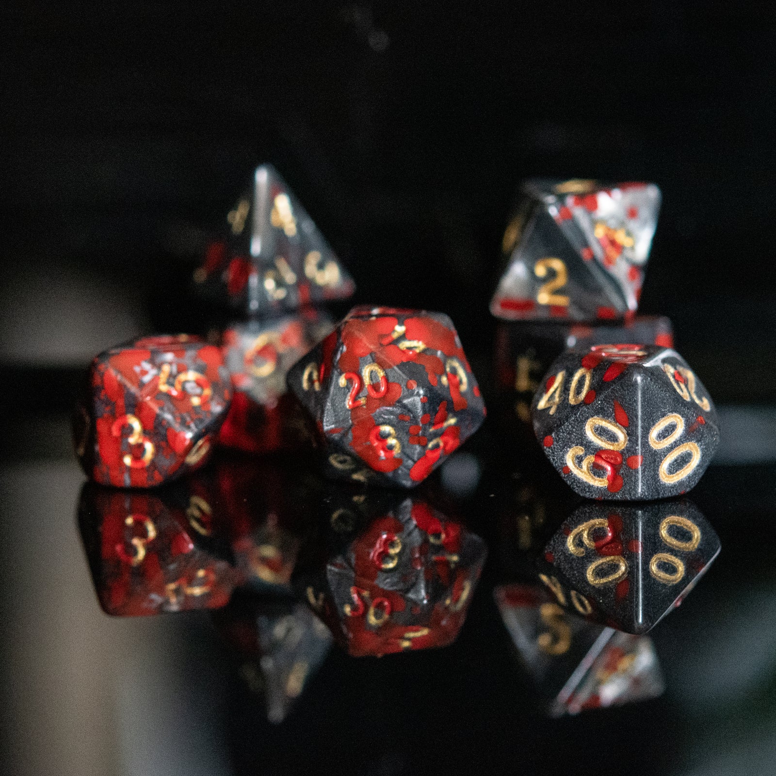 A set of acrylic dice with red and black colors and gold numbers, reflecting on a shiny surface.