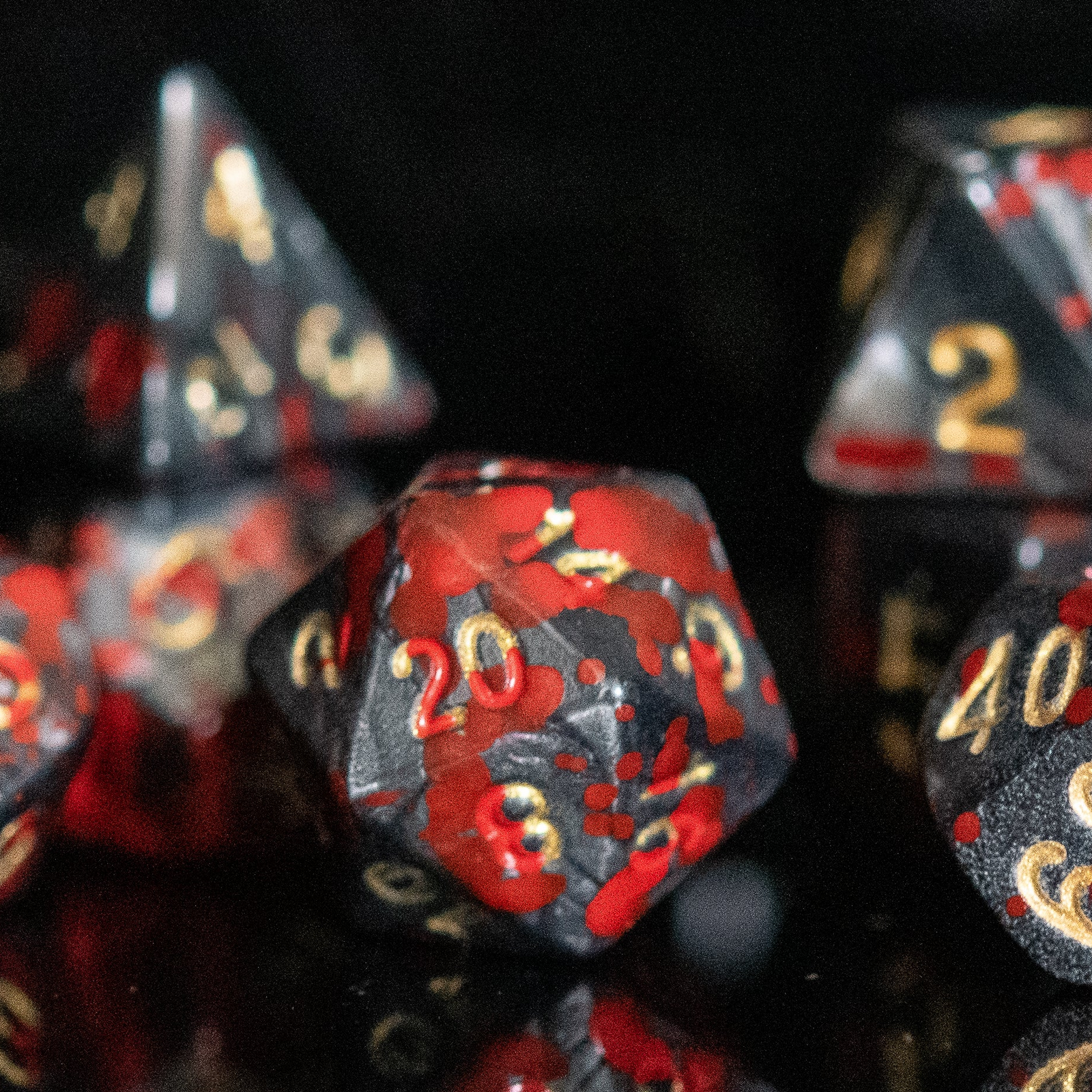A set of acrylic dice with red and black colors and gold numbers, reflecting on a shiny surface. 