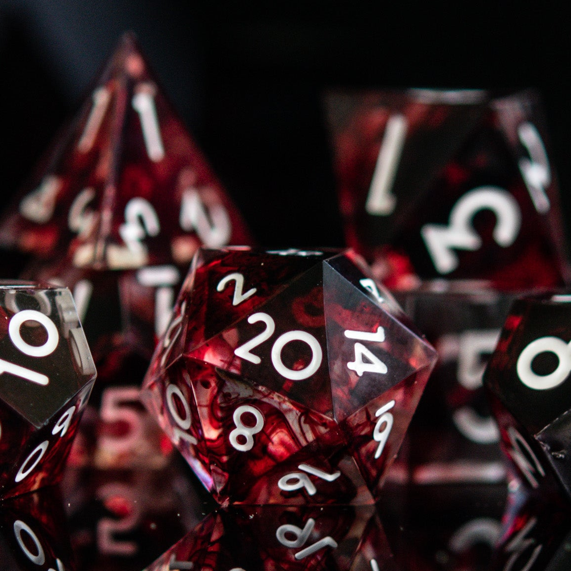 A set of polyhedral sharp edge resin clear dice with blood red running through and white numbering for tabletop games and board games