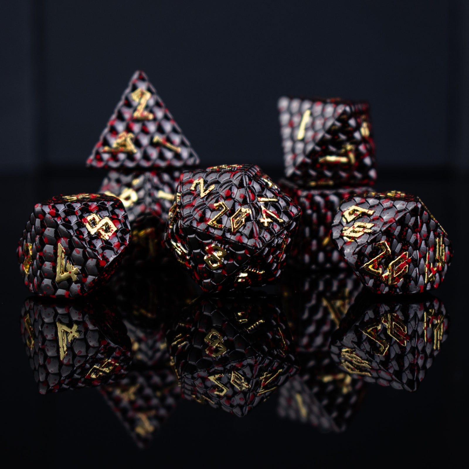 A set of solid metal black dragon scale textured polyhedral dnd dice splattered with blood with gold numbers