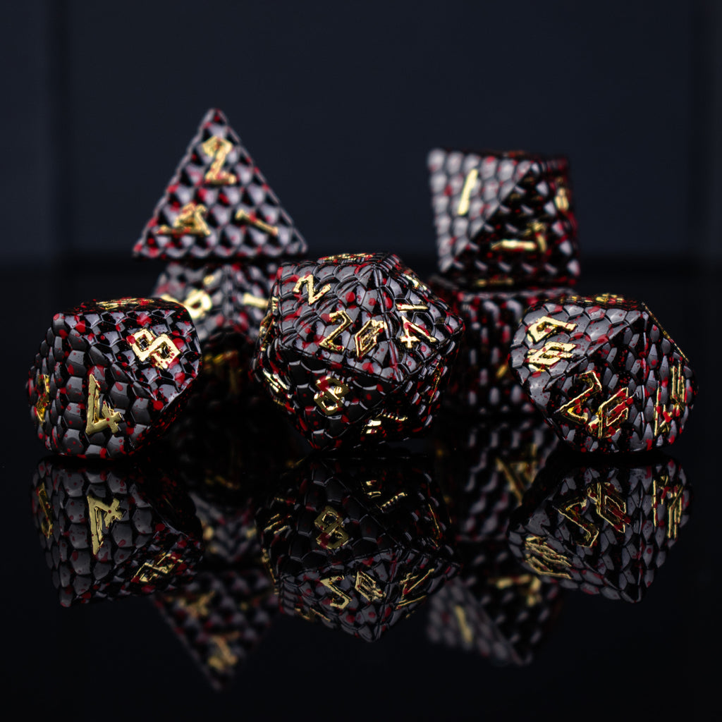 A set of solid metal black dragon scale textured polyhedral dnd dice splattered with blood with gold numbers