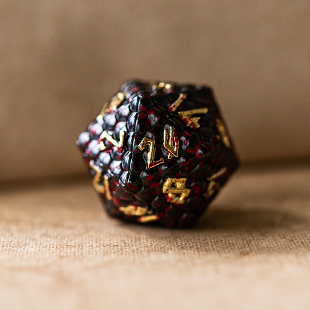 A set of solid metal black dragon scale textured polyhedral dnd dice splattered with blood with gold numbers