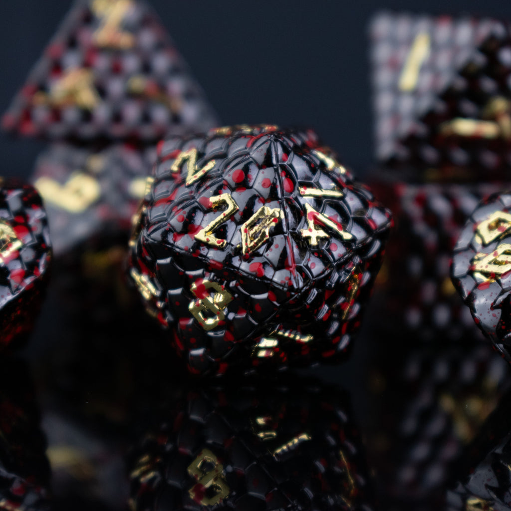 A set of solid metal black dragon scale textured polyhedral dnd dice splattered with blood with gold numbers
