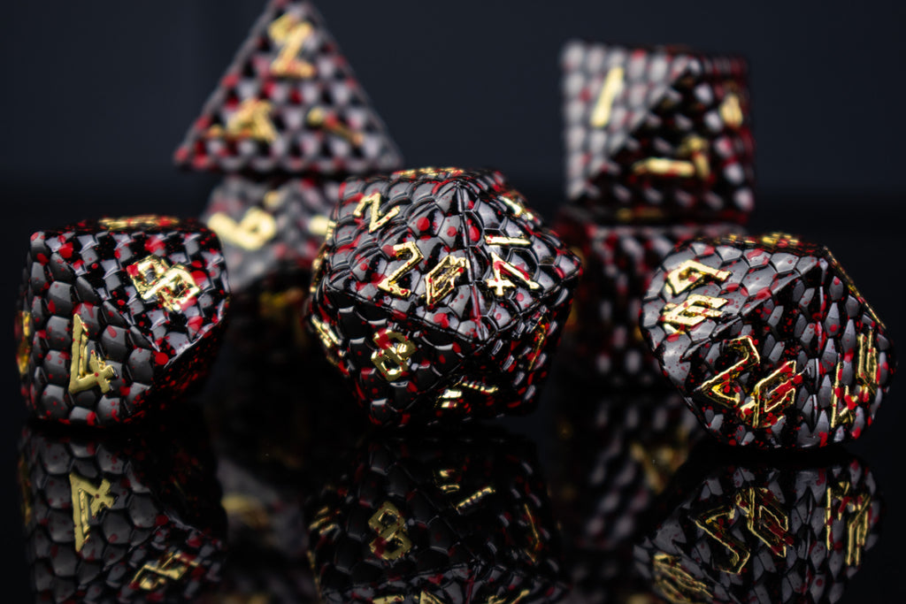 A set of solid metal black dragon scale textured polyhedral dnd dice splattered with blood with gold numbers