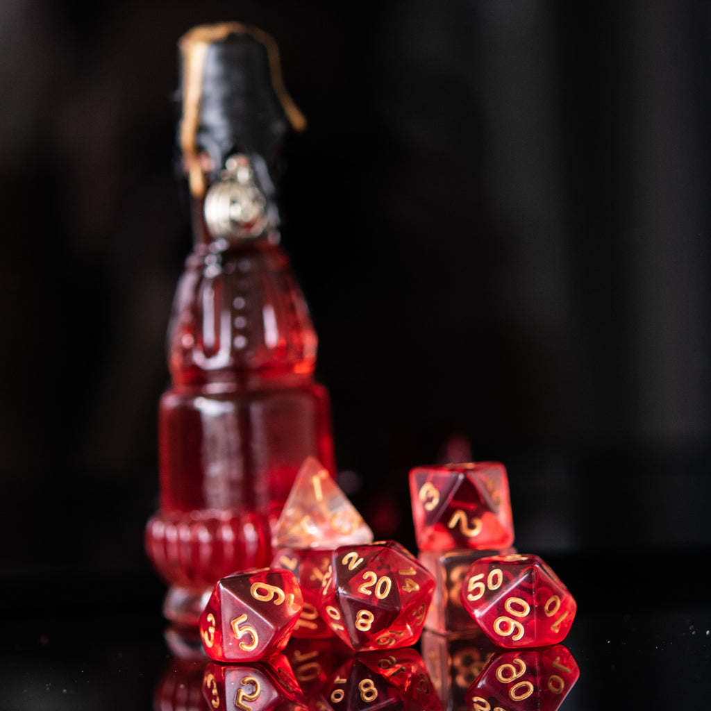 A set of red acrylic dice with engraved numbers, displayed alongside a bottle-shaped container with a stopper, against a black background.