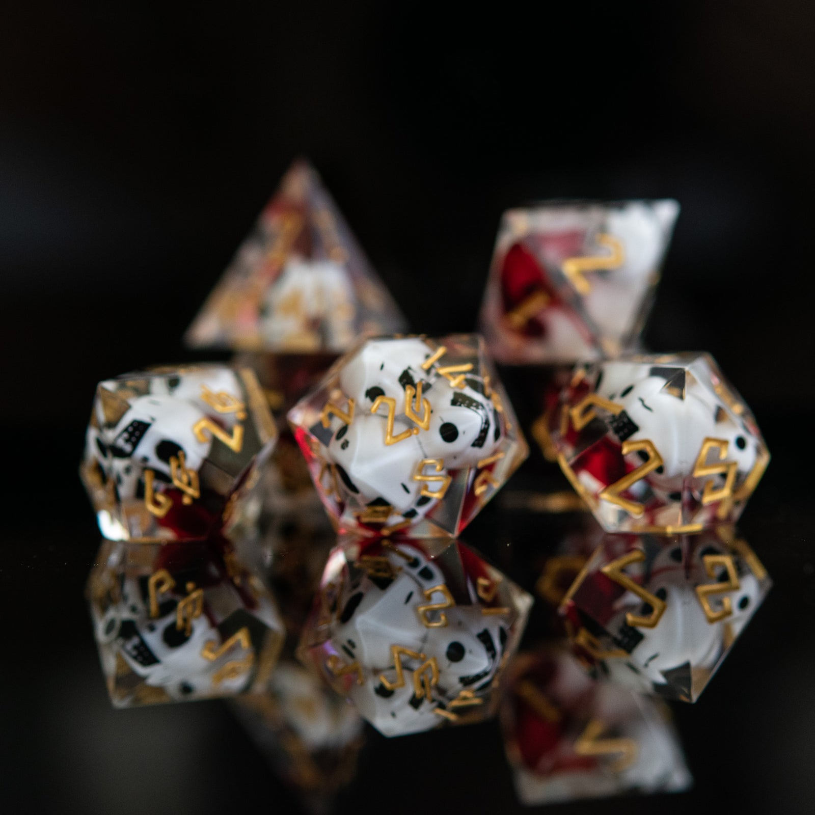 A set of clear sharp-edged resin dice with engraved numbers in gold, with white skulls and red blood inside including various shapes such as a d4, d6, d8, d10, d12, and d20 for tabletop and board games